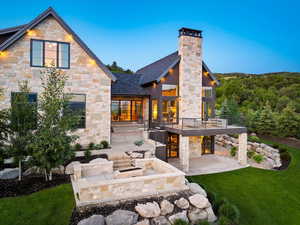 Back of property with stone siding, a patio, a yard, and a chimney