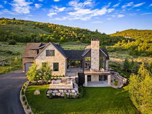 View of front of home with stone siding, a view of trees, driveway, a patio, and a chimney