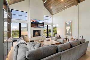 Living area featuring high vaulted ceiling, wood ceiling, a fireplace, light wood-style flooring, and healthy amount of natural light