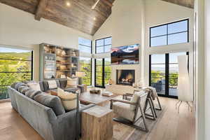Living room with high vaulted ceiling, a wooden ceiling with exposed beams, light wood-style floors, a fireplace, and plenty of natural light