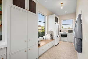 Kitchen featuring high end white fridge, brick patterned flooring, white cabinets, light countertops, and glass insert cabinets