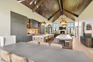 Dining room featuring a wooden ceiling with exposed beams, high vaulted ceiling, light wood-type flooring, a lit fireplace, and a ceiling fan