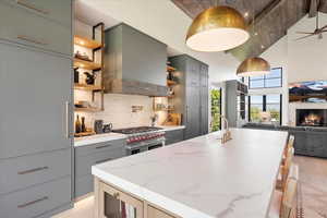 Kitchen with open shelves, wall chimney exhaust hood, gray cabinets, range with two ovens, and high vaulted ceiling