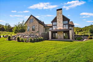 Rear view of property with stone siding, a balcony, a patio area, a yard, and a chimney
