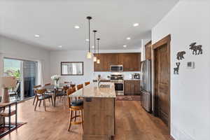 Kitchen with stainless steel appliances, recessed lighting, a kitchen bar, a kitchen island with sink, and light stone counters