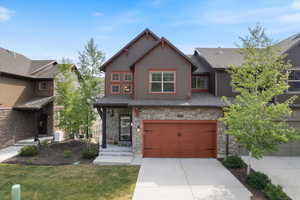View of front of home with stone siding, concrete driveway, an attached garage, a front lawn, and a shingled roof