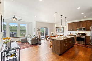 Kitchen featuring stainless steel appliances, open floor plan, light stone counters, a breakfast bar, and dark wood-style floors