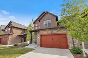 View of front facade featuring stone siding, a garage, and driveway