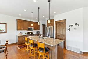 Kitchen with appliances with stainless steel finishes, dark wood finished floors, a center island with sink, a breakfast bar area, and recessed lighting