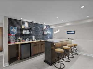 Indoor wet bar with fridge, finished concrete flooring, recessed lighting, and backsplash