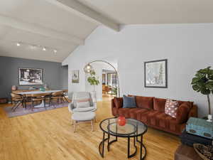 Living room with light wood finished floors, beamed ceiling, track lighting, and high vaulted ceiling
