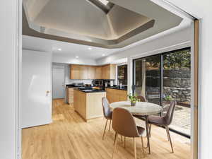 Kitchen featuring light brown cabinets, stainless steel microwave, a kitchen island, dark countertops, and a raised ceiling