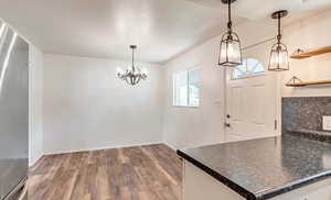 Kitchen featuring dark wood finished floors, a chandelier, open shelves, dark countertops, and hanging light fixtures