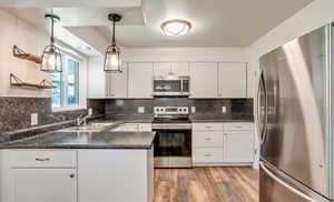 Kitchen featuring stainless steel appliances, dark countertops, and white cabinetry