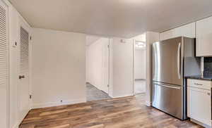 Kitchen with freestanding refrigerator, light wood finished floors, white cabinets, and dark stone countertops