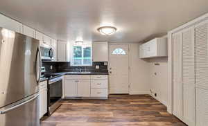 Kitchen featuring appliances with stainless steel finishes, dark countertops, white cabinetry, tasteful backsplash, and dark wood finished floors