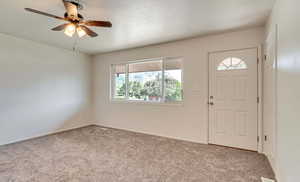 Carpeted entryway with ceiling fan and baseboards