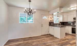 Kitchen featuring appliances with stainless steel finishes, a chandelier, dark countertops, decorative backsplash, and dark wood-style floors