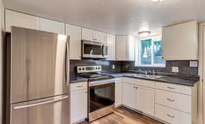 Kitchen with stainless steel appliances, dark countertops, white cabinets, decorative backsplash, and a textured ceiling