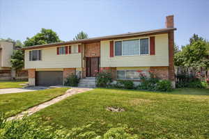Split foyer home featuring brick siding, driveway, a garage, and a chimney