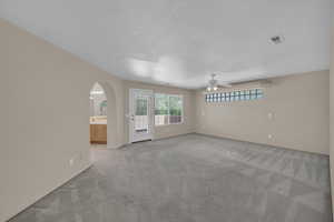 Spare room featuring a ceiling fan, light carpet, plenty of natural light, arched walkways, and a textured ceiling