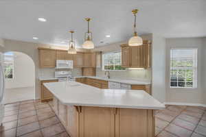Kitchen featuring white appliances, a kitchen island with sink, light countertops, light brown cabinetry, and a textured ceiling