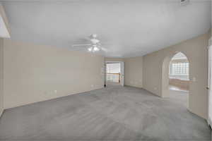 Unfurnished room with arched walkways, ceiling fan, and light carpet