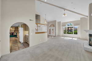 Unfurnished living room featuring a multi sided fireplace, high vaulted ceiling, carpet floors, a ceiling fan, and arched walkways