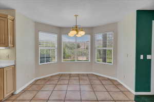 Unfurnished dining area featuring a chandelier, light tile patterned floors, and a textured ceiling