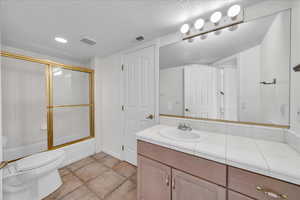 Full bath featuring vanity, a textured ceiling, combined bath / shower with glass door, and tile patterned floors