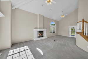 Unfurnished living room with high vaulted ceiling, ceiling fan, plenty of natural light, and carpet