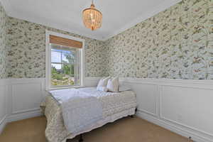 Bedroom with a chandelier, ornamental molding, wallpapered walls, wainscoting, and a decorative wall