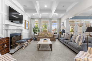 Carpeted living room featuring a decorative wall, crown molding, beam ceiling, coffered ceiling, and a fireplace with flush hearth