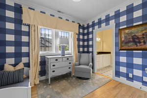 Sitting room with wallpapered walls, light wood-style flooring, and crown molding