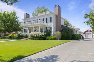 View of front of home featuring a chimney, a balcony, a front lawn, and concrete driveway
