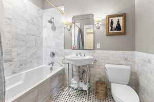 Full bathroom with tile walls, tiled shower / bath, a wainscoted wall, and tile patterned flooring