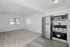 Kitchen with stainless steel appliances, white cabinetry, light wood finished floors, and light countertops