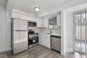 Kitchen with appliances with stainless steel finishes, white cabinets, light wood-style floors, and light stone countertops