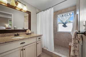 Ensuite bathroom with healthy amount of natural light, a tile shower, and vanity