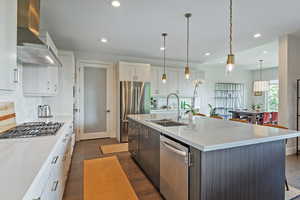 Kitchen with wall chimney exhaust hood, appliances with stainless steel finishes, dark wood finished floors, light countertops, and recessed lighting