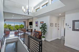 Hall featuring a high ceiling, healthy amount of natural light, dark wood finished floors, a chandelier, and recessed lighting