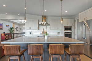 Kitchen featuring island exhaust hood, stainless steel appliances, recessed lighting, decorative backsplash, and light countertops