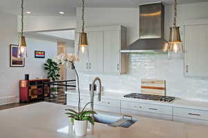 Kitchen with wall chimney range hood, stainless steel gas cooktop, light countertops, decorative backsplash, and recessed lighting