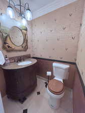 Half bath featuring vanity, crown molding, tile patterned floors, and wallpapered walls