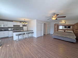 Kitchen with white appliances, dark countertops, a breakfast bar area, open floor plan, and white cabinets