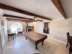 Playroom with a textured wall, pool table, a ceiling fan, beamed ceiling, and a textured ceiling