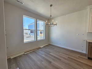 Unfurnished dining area featuring a chandelier, wood finished floors, and a textured ceiling