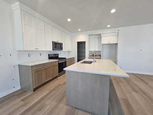 Kitchen with appliances with stainless steel finishes, light wood-style floors, white cabinets, an island with sink, and recessed lighting