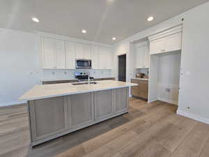 Kitchen featuring stainless steel appliances, white cabinets, a center island with sink, light wood-style flooring, and recessed lighting