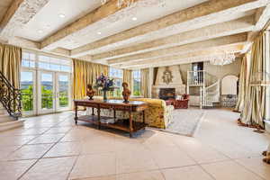 Living room with stairway, light tile patterned floors, a high end fireplace, beamed ceiling, and a chandelier